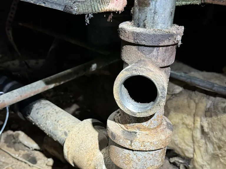 What we found under an older bathroom once the floor was open: old drain lines in the crawl space (left) and a corroded cast-iron fitting (right).