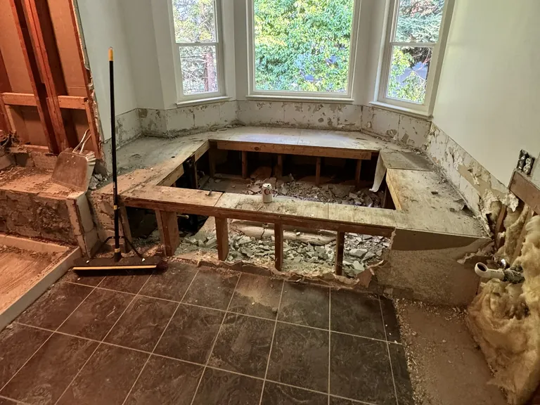 What nobody can price from photos: a primary bathroom after demolition, with the old tub deck open (left) and the drains and supply lines exposed in the wall (right).