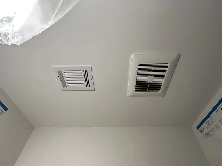 A new fan housing wired before it goes into the ceiling (left), and the finished fan grille next to a heating register (right).