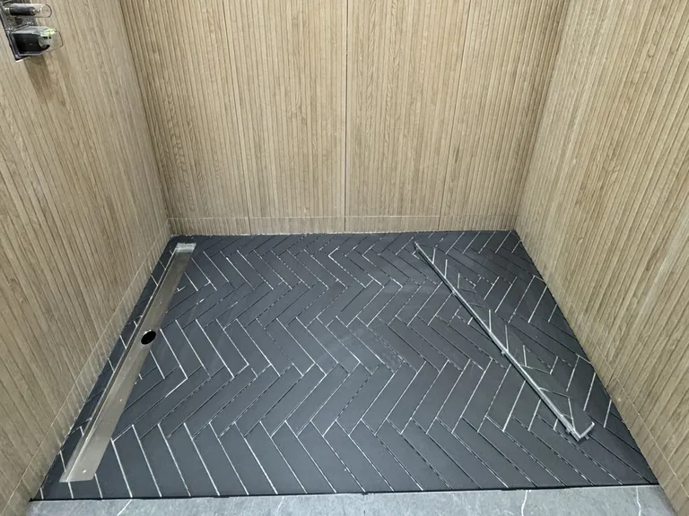 A linear drain along the back wall of a tiled shower floor, so the floor can slope in one direction.