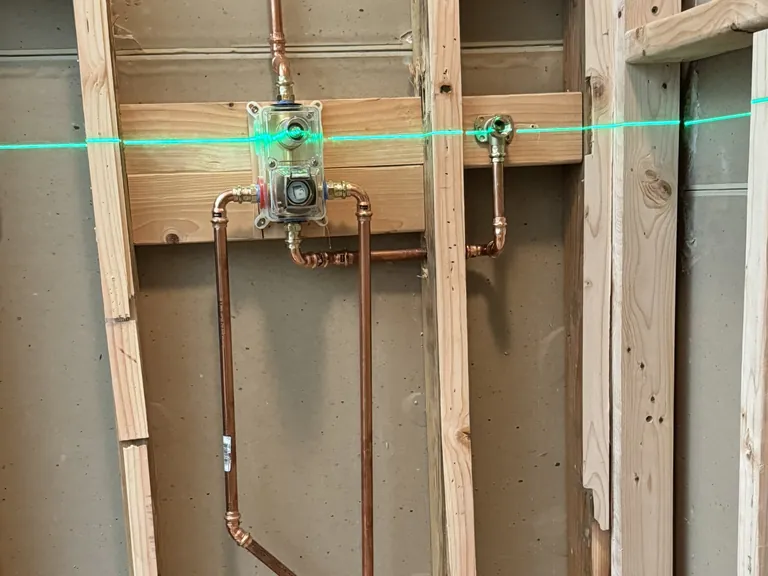 A shower valve body set on solid blocking during rough plumbing, with the line to the showerhead running up from it.