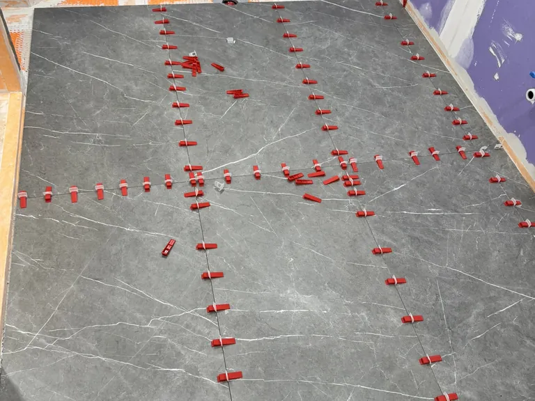 Large-format porcelain: mortar spread on the back of each tile for full contact (left), and leveling clips at every joint so the edges sit flush (right).